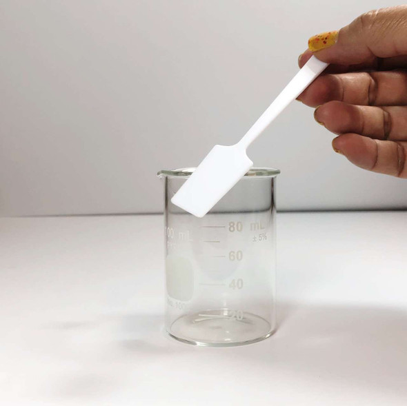 A hand holding a white long plastic spatula on top of a beaker.