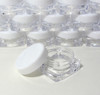 Stacks of small square cosmetic sample jars with white caps