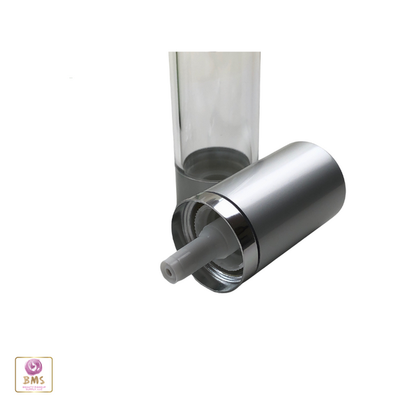 An empty clear airless bottle with the airless pump sitting on its side next to the bottle.