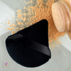 A top view of a black triangle velvet powder puff with strap with a bottle of loose makeup powder