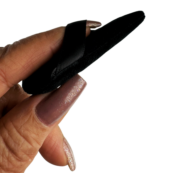 A finger through a strap of a thin black powder puff